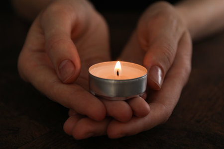Woman holding burning tealight candle on black background, closeupの写真素材