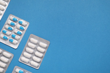 Different antibiotic pills in blisters on light blue background, flat lay. Space for textの写真素材