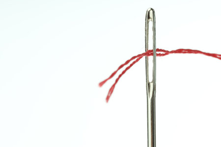 Sewing needle with red thread on white background, closeup