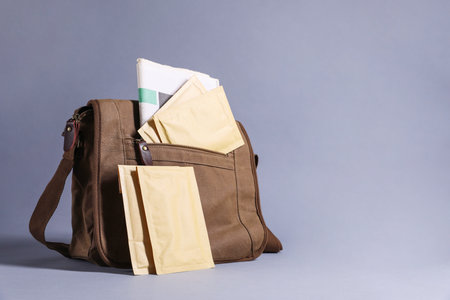 Brown postman's bag with envelopes and newspapers on gray background. Space for textの写真素材