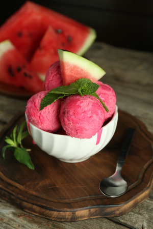 Scoops of tasty watermelon sorbet in bowl, fresh fruit, mint and spoon on wooden tableの写真素材