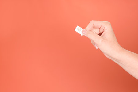 Woman holding SIM card on terracotta background, closeup. Space for textの写真素材
