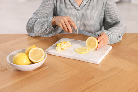 Making lemon water. Woman cutting fruit at wooden table indoors, closeupの写真素材