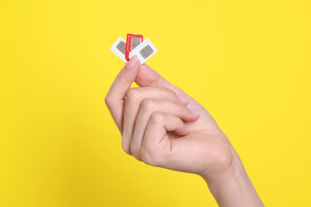 Woman holding SIM cards on yellow background, closeup