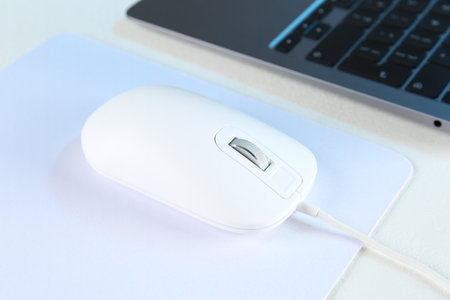 Computer mouse with mousepad and laptop on white table, closeup