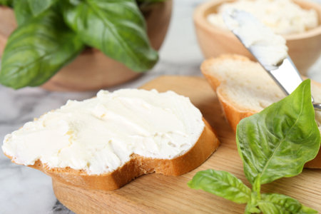 Pieces of bread with cream cheese and basil leaves on white table, closeupの写真素材