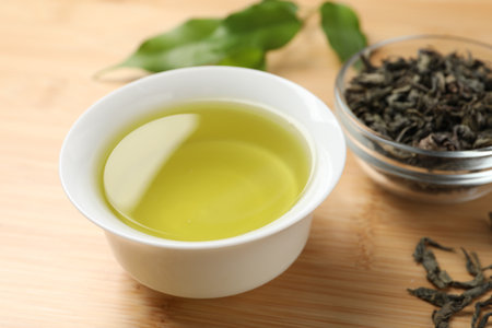 Refreshing green tea in cup and leaves on wooden table, closeupの写真素材
