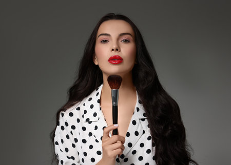 Beautiful makeup. Attractive woman with brush on grey backgroundの写真素材