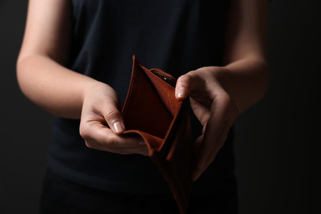 Woman with empty wallet on dark background, closeup