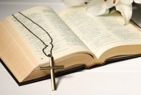 Cross with chain and Bible on white wooden table, closeup. Religion of Christianity