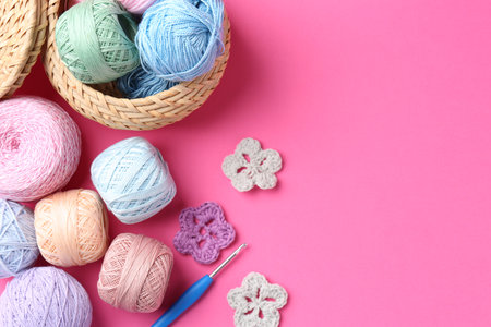 Different colorful yarns, crochet flowers and hook on pink background, flat lay. Space for textの写真素材