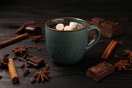 Tasty melted chocolate with marshmallows in cup and spices on dark wooden table, closeupの写真素材