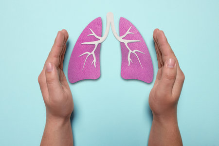 Woman holding hands near illustration of lungs on light blue background, closeup. Asthma and other respiratory diseasesの写真素材