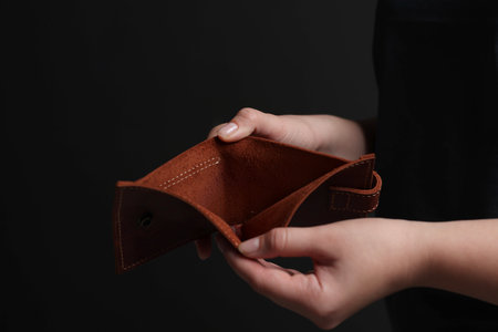 Woman with empty wallet on dark background, closeup