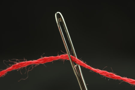 Sewing needle with red thread on black background, closeupの写真素材