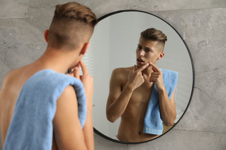 Man with towel touching his face near mirror in bathroomの写真素材
