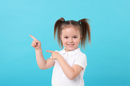 Portrait of happy little girl pointing at something on light blue backgroundの写真素材
