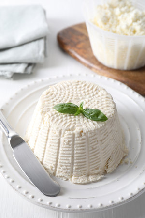 Fresh ricotta (cream cheese) with basil and knife on white tableの写真素材