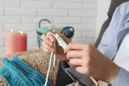 Woman crocheting with hook and yarn at home, closeup