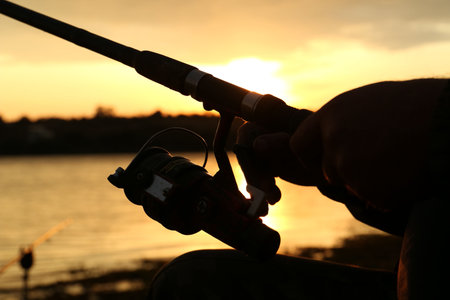 Fisherman with rod fishing near lake at sunset, closeupの写真素材
