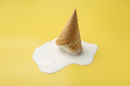 Melted ice cream in wafer cone on yellow backgroundの写真素材