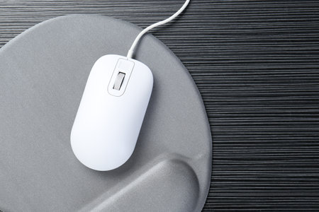 Computer mouse and mousepad with armrest on black wooden table, top view. Space for text