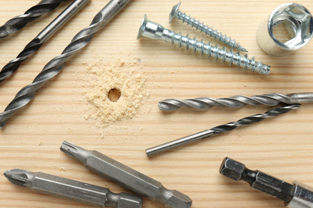 Different drill bits on holed wooden surface, flat lay