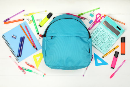 Backpack and different school supplies on white wooden background, flat lay