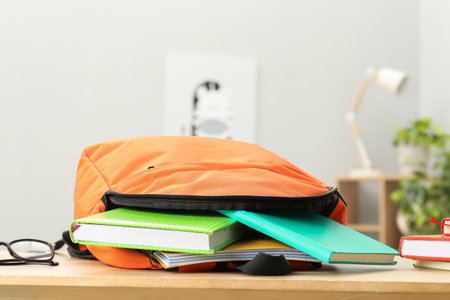 Backpack and different school stationery on wooden table indoors