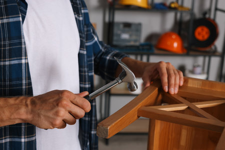 Man repairing wooden stool with hammer indoors, closeupの写真素材