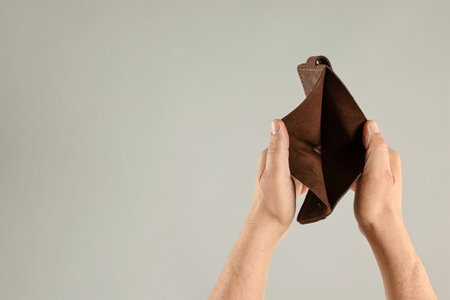 Man with empty wallet on gray background, closeup. Space for text