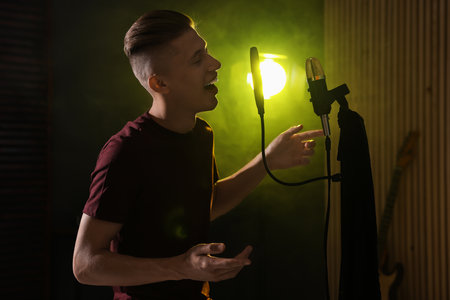 Vocalist singing into microphone in professional record studio with smoke and lightsの写真素材