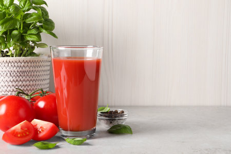 Tasty tomato juice in glass, basil leaves, peppercorns and fresh vegetables on light grey table, space for textの写真素材