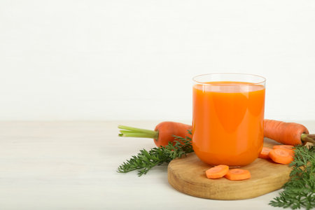 Fresh carrot juice in glass and vegetables on light wooden table against white background. Space for textの写真素材