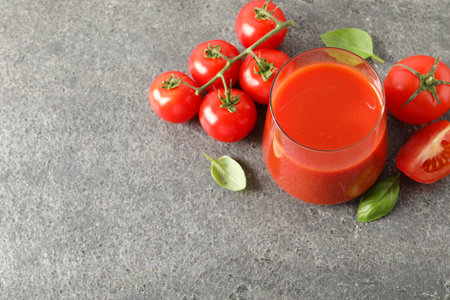 Tasty tomato juice in glass, basil and fresh vegetables on grey table, above view. Space for textの写真素材