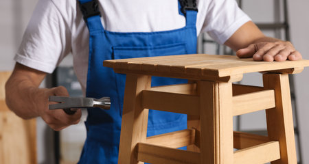 Man repairing wooden stool with hammer indoors, closeupの写真素材