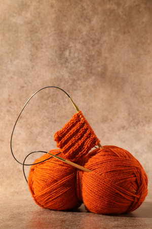 Skein of orange yarn, knitted fabric and needles on light brown background, space for text