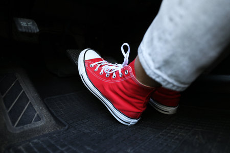 Woman in sneakers pushing on pedal of car brake, closeupの写真素材