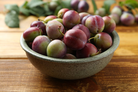 Ripe plums in bowl on wooden table, closeupの写真素材