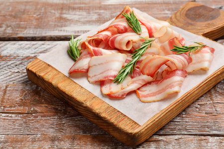 Slices of raw bacon and rosemary on wooden tableの写真素材