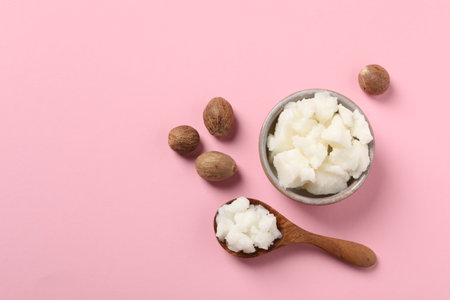 Shea butter in bowl, spoon and nuts on pink background, flat lay. Space for textの写真素材