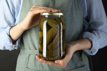Woman with jar of tasty pickled cucumbers on gray background, closeup
