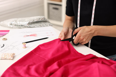 Fashion designer cutting pink fabric at table in workshop, closeupの写真素材