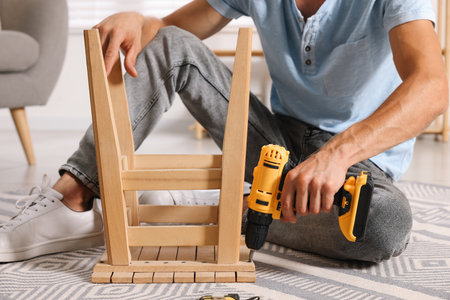 Man repairing wooden stool with electric screwdriver indoors, closeupの写真素材