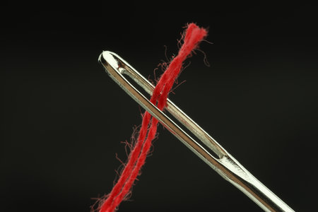 Sewing needle with red thread on black background, closeup