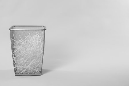 Shredded paper strips in trash bin on light grey background, space for text