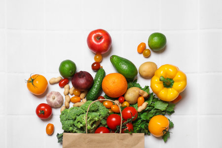 Vegan food delivery. Paper bag with different fresh vegetables, nuts and fruits on white tiled table, flat layの写真素材
