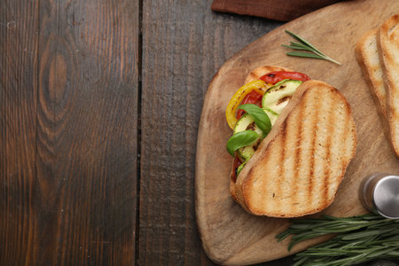 Tasty sandwich with grilled vegetables, rosemary and spices on wooden table, top view. Space for textの写真素材