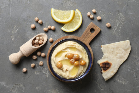 Delicious hummus with olive oil, chickpeas, lemon and pita on gray textured table, flat layの写真素材