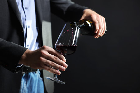 Man pouring red wine from bottle into glass on black background, closeup. Space for textの写真素材